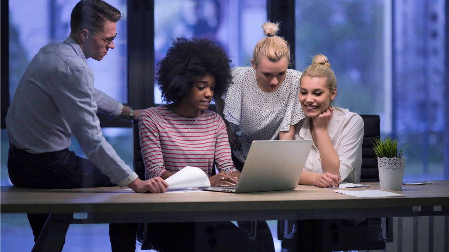 Four people sitting and looking at a laptop