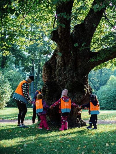 Children in bright orange vests circling a tree. - Jussi Hellsten / Helsinki Partners