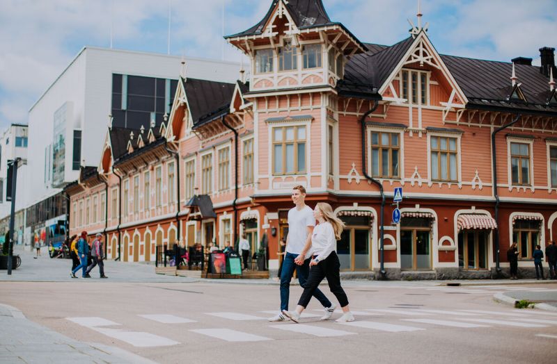 A couple crosses the street in front of a pink Victorian building. - Julia Kivelä / Business Finland