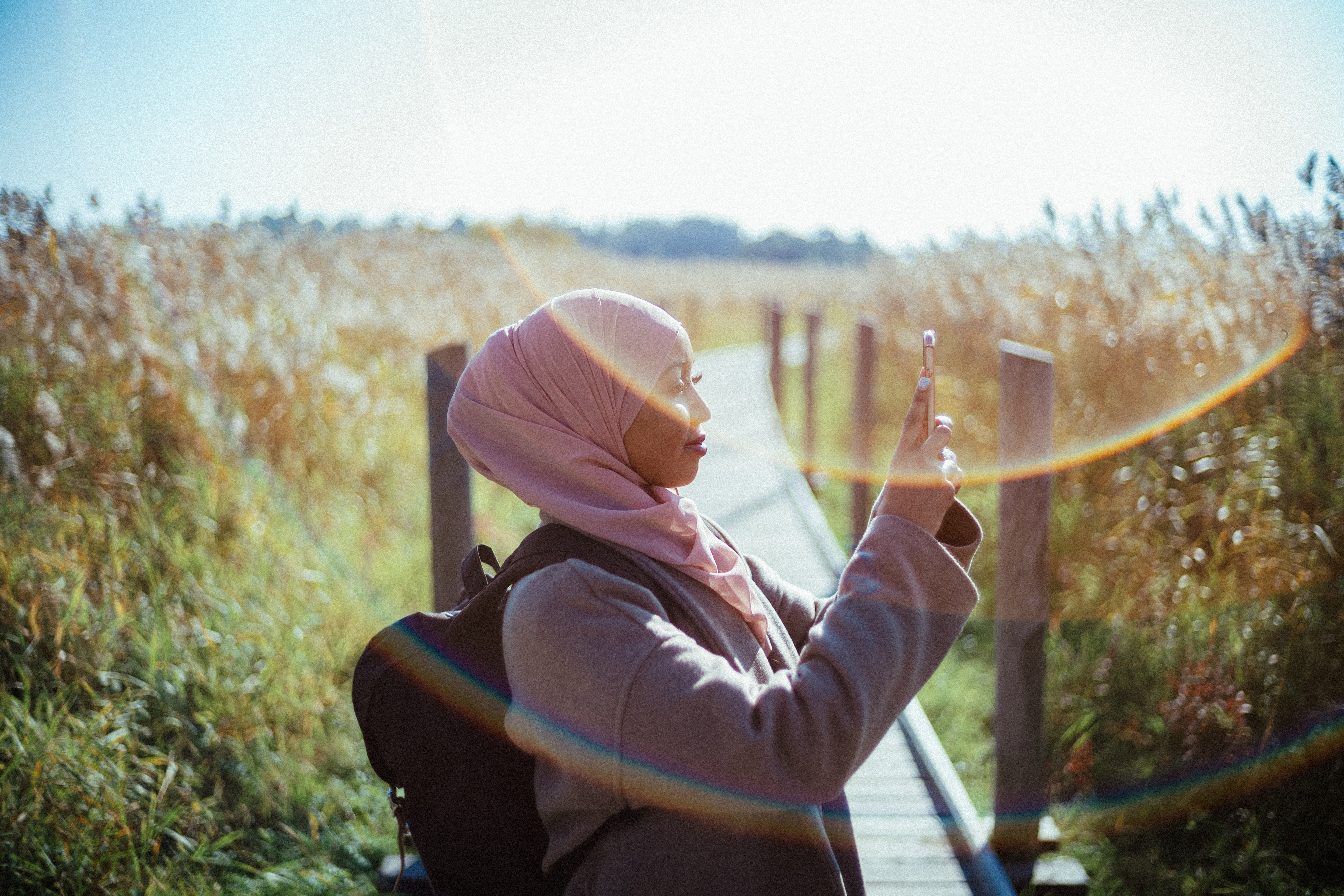 a woman standing on duckboards and taking a picture of a bed of reeds with her phone