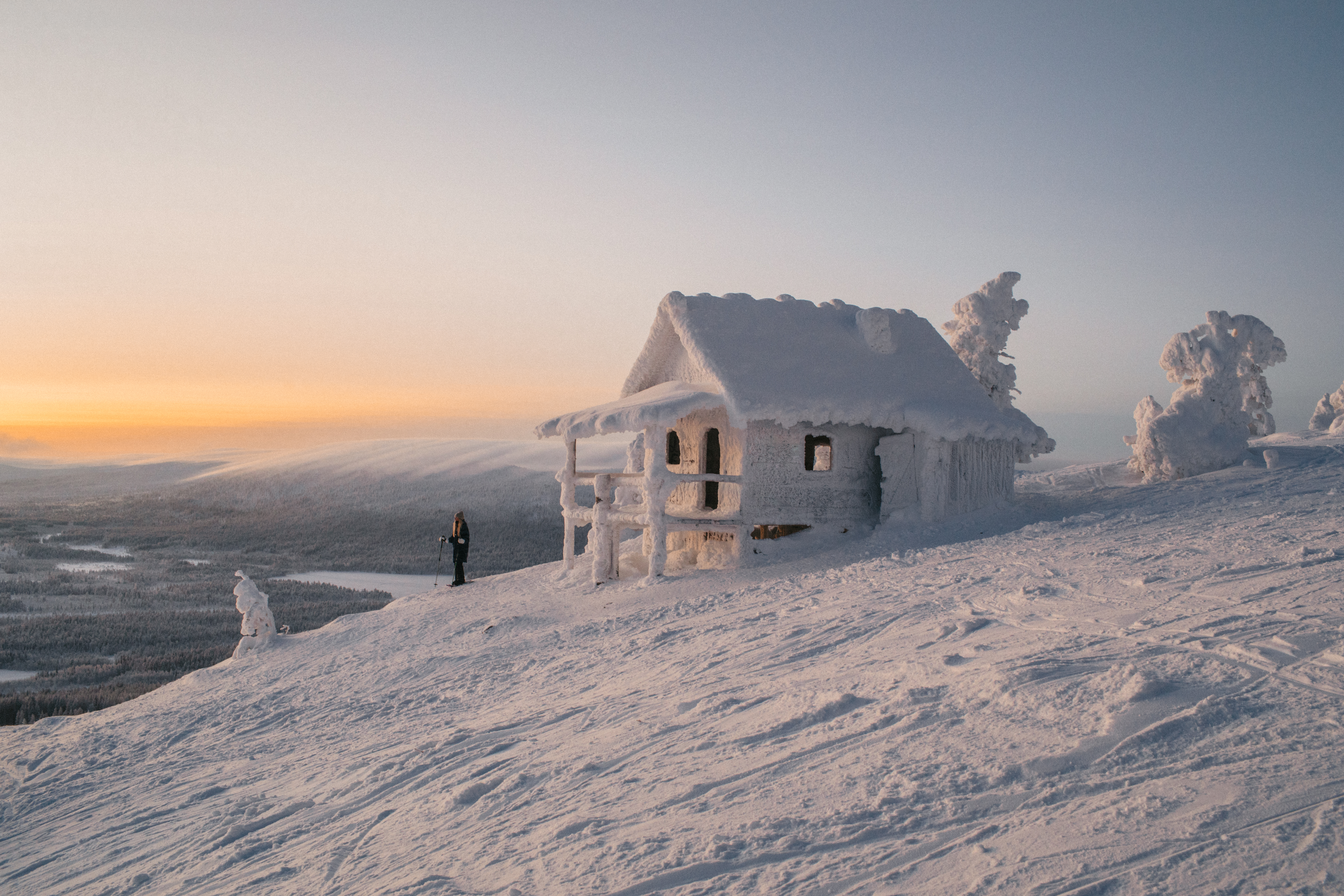 an snowshoeer next to a hut completely covered in ice and snow on top of a fell