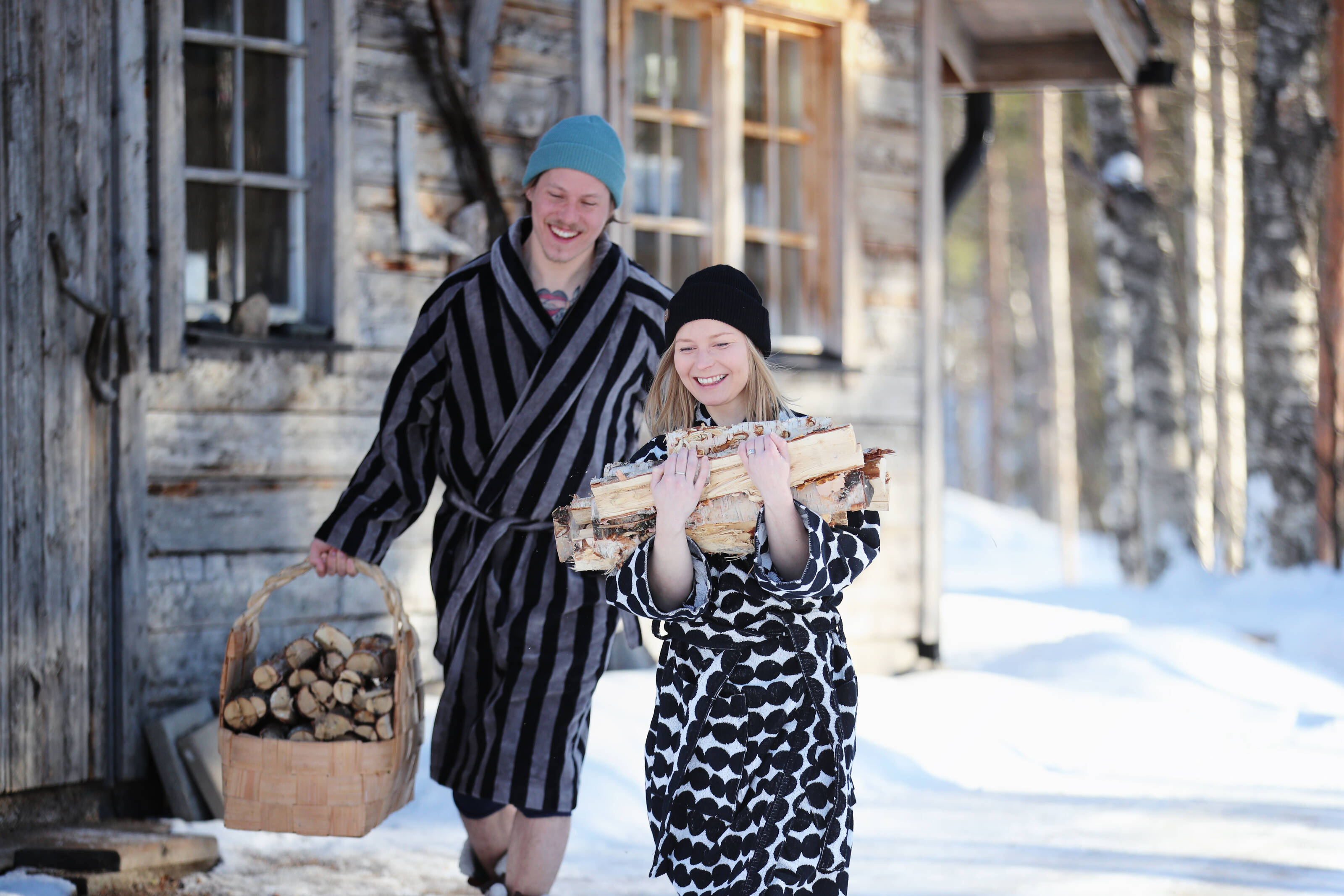 A young couple is carrying firewood to a sauna in snow