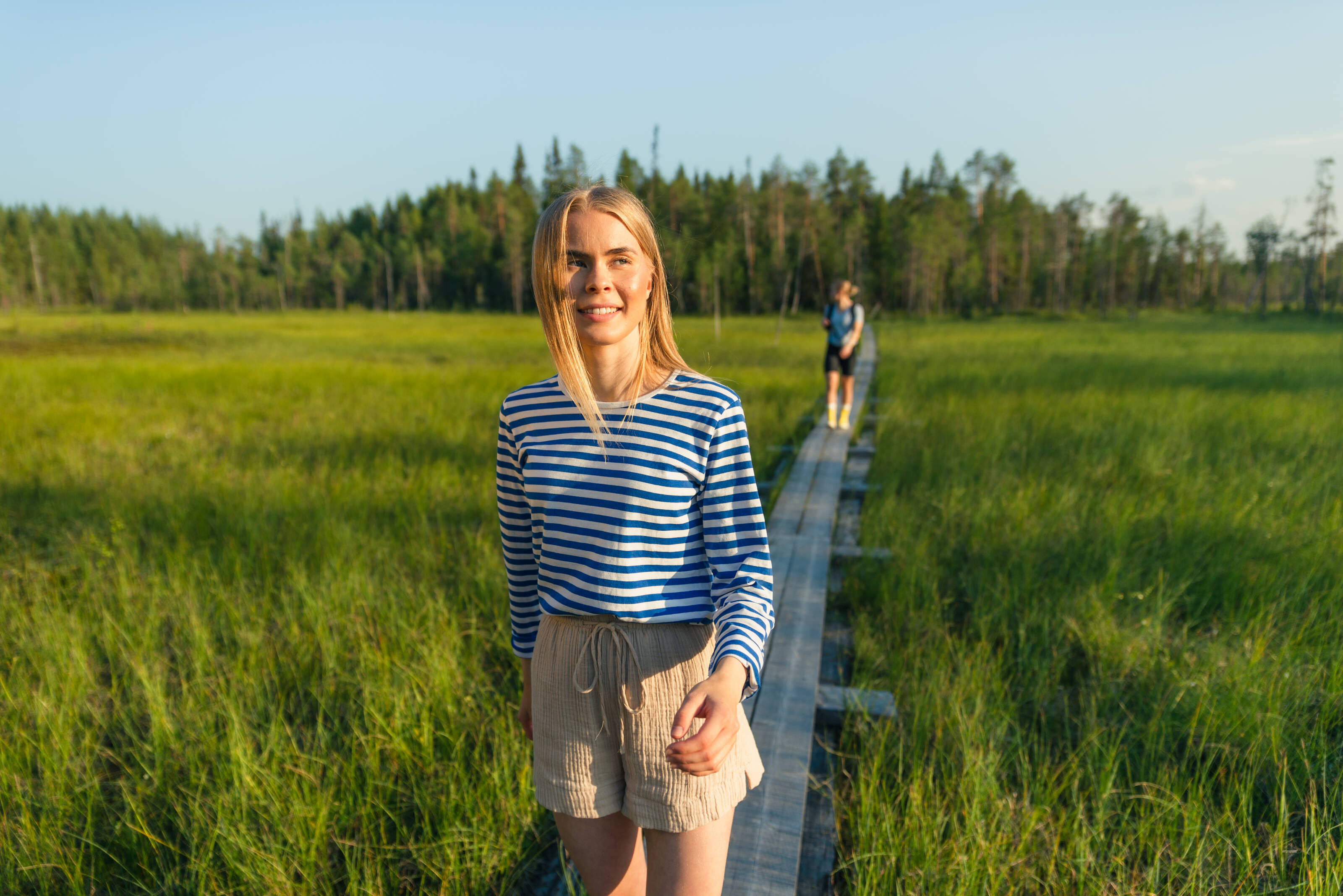 Two women walking on a wooden path in a Finnish cloudberry swamp.