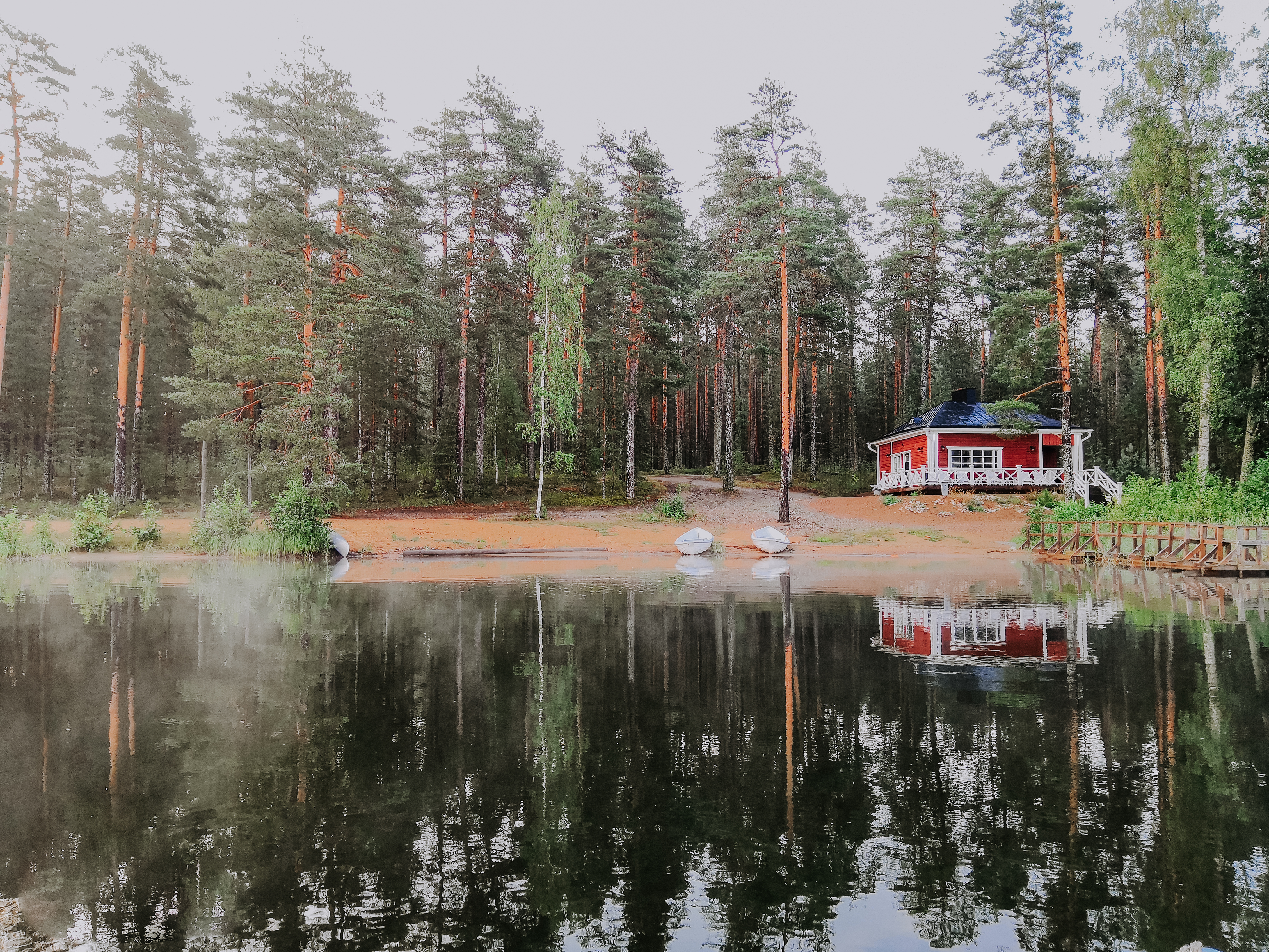 an idyllic red wooden building at the lake in the middle of a forest