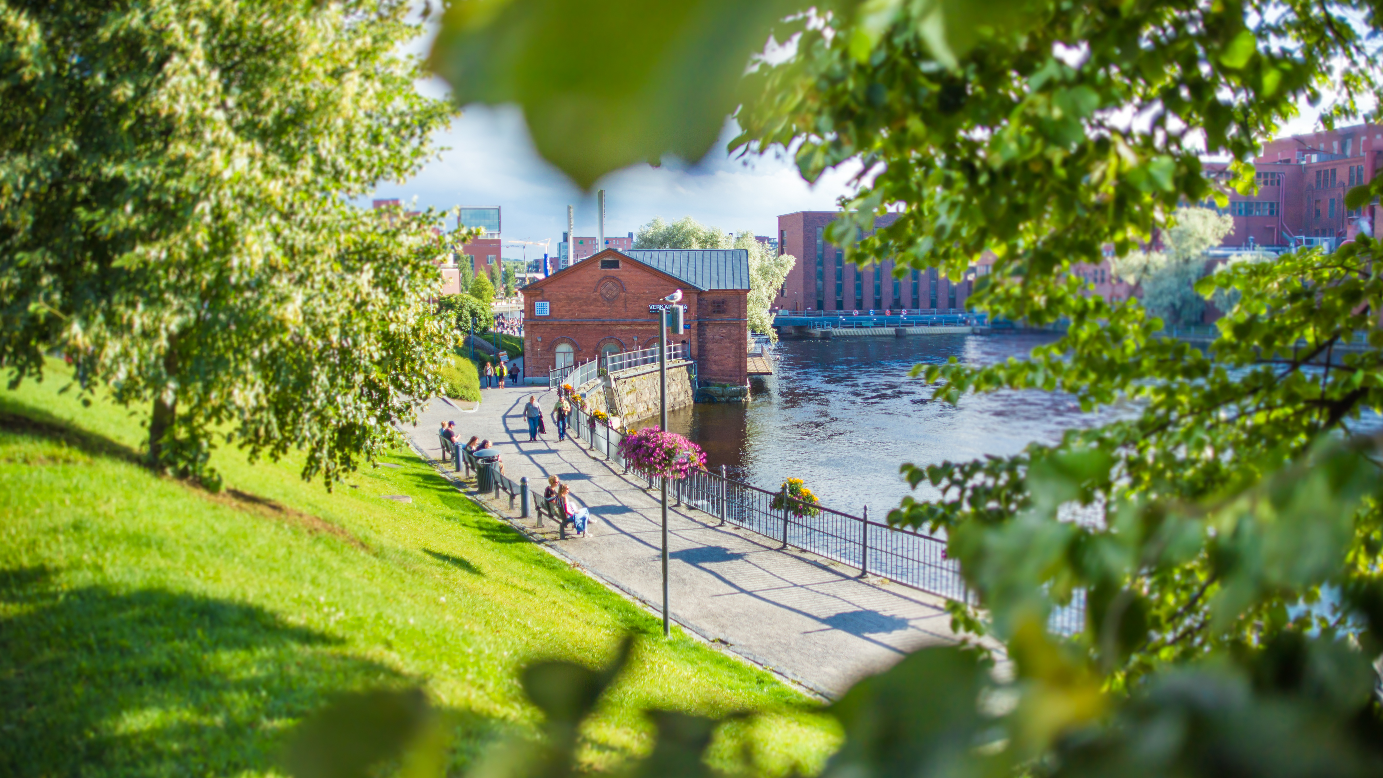 a sunny park on the shore of the Tammerkoski rapid full of people in Tampere