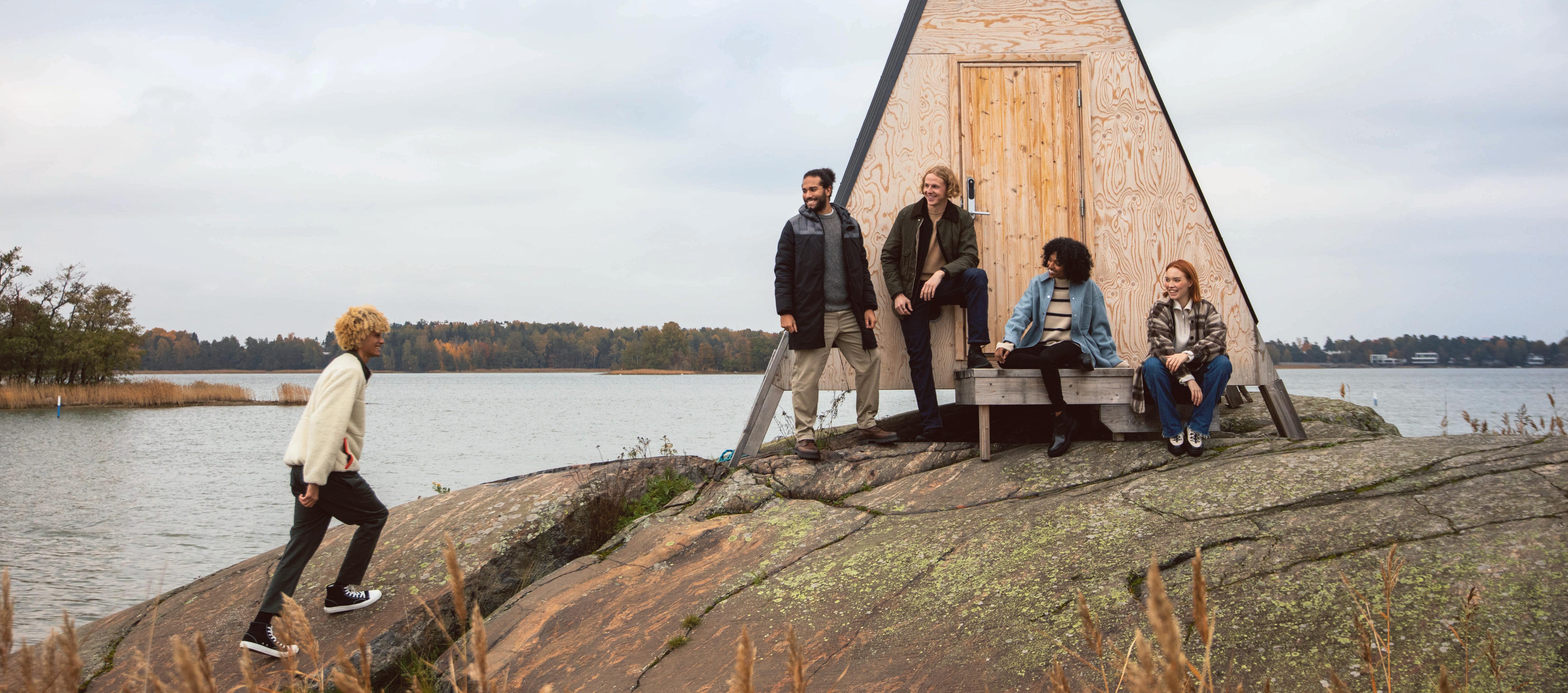 a group of young people on the shores of the Baltic Sea in front of a Nolla-Cabin welcoming a friend